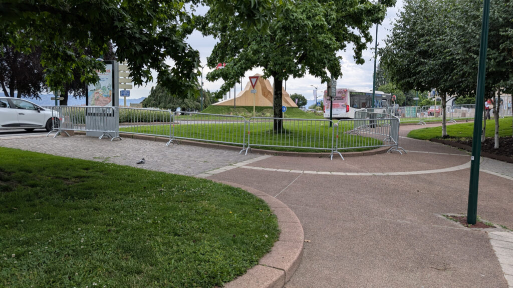 Barrières de sécurité métalliques délimitant un espace public à Évian-les-Bains, structure pyramidale en bois et bus en arrière-plan